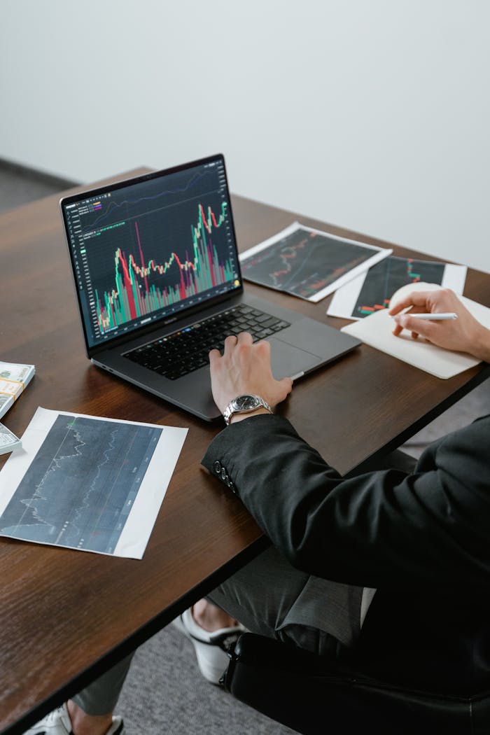 A business analyst reviewing stock charts on a laptop, analyzing market trends.